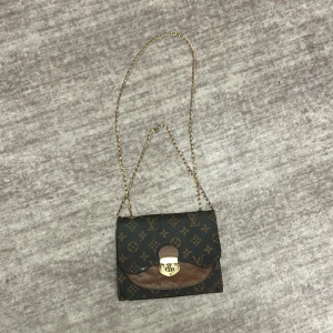 Mönstrad axelväska med kedja - Snygg axelväska med ett klassiskt mönster och guldfärgad kedja. Väskan har en elegant låsdetalj framtill och en stilren design som passar perfekt för olika tillfällen.