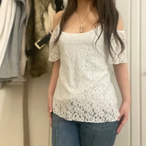 Vit spetsblus - Säljer en söt vit spetsblus med offshoulder-design. Blusen har korta ärmar och ett vackert blommönster. Perfekt för en somrig look!