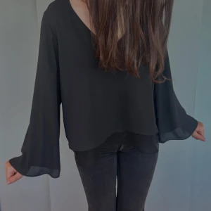 Svart blus med v-ringning - Elegant svart blus med v-ringning och långa, fladdriga ärmar. Perfekt för en stilren look. Storlek: passar både xs och s. 