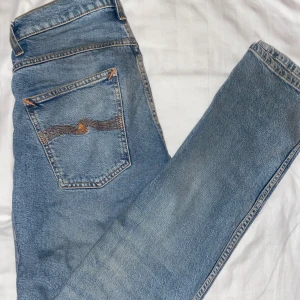 Blå jeans från Nudie Jeans - Snygga blå jeans från Nudie Jeans med klassisk femficksdesign och orange sömmar. Jeansen har en normal passform och är tillverkade i slitstarkt denim. Perfekta för en avslappnad stil.