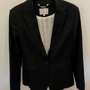 Mörkblå randig kavaj från Stockh LM - Elegant mörkblå kavaj från Stockh LM med diskreta ränder och klassisk design. Kavajen har en knapp framtill och tre knappar vid ärmsluten. Perfekt för en stilren look.