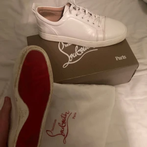 Vita sneakers från Christian Louboutin lite amutsiga under som ni kan se storlek 44 - Snygga vita sneakers från Christian Louboutin med den ikoniska röda sulan. Skorna har snörning och är tillverkade i skinn, vilket ger en lyxig känsla. Perfekta för den som vill ha stilrena och exklusiva skor. storlek 44 utan taggar
