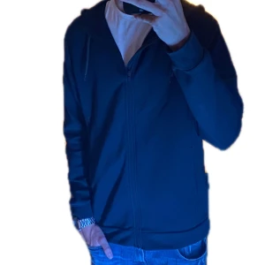 Fullzip från dressman - Säljer en stilren mörkblå hoodie från Dressmann👔🍾. Den har dragkedja framtill och en praktisk huva med snörning🥂⚡️. Perfekt för en avslappnad look. ⭐️🤩Storlek M men sitter som M/L så passar större storlekar med.💍🕶️ Helt ny ingen defekt på den.🆕🧥 Ny pris 699 mitt pris 380. Skriv för fler frågor och bilder. Kan också tänka mig att byta mot något så kom gärna med bytesförslag.🍻👟