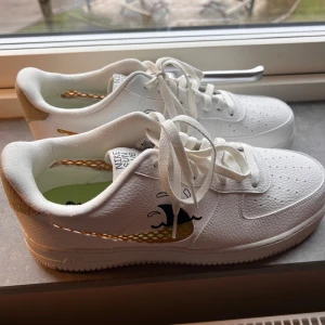 Oanvända vita Nike Sun Club sneakers - Aldrig använda vita Nike Sun Club sneakers med unika detaljer som inte säljs längre. Skorna har en vågdesign på sidan och en beige häl. Innersulan är grön med ett blommönster. Perfekta för en stilren look.