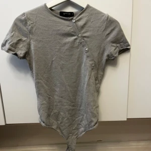 Grå/blå ribbad bodysuit  - Säljer en grå/blå  ribbad bodysuit med korta ärmar och knappar framtill. Perfekt för en stilren och bekväm look. Passar bra till både jeans och kjol.