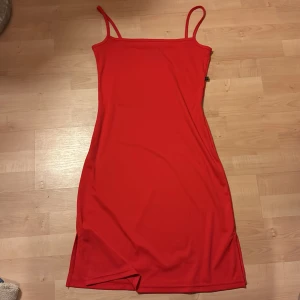 Röd klänning från Sparkz - Snygg röd klänning från Sparkz med smala axelband och en enkel design. Perfekt för en stilren look. Klänningen har en slits på sidan som ger en extra touch.