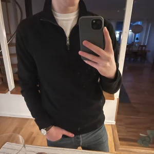 Svart tröja med dragkedja - Snygg svart tröja med dragkedja i kragen. Tröjan har långa ärmar och en bekväm passform.