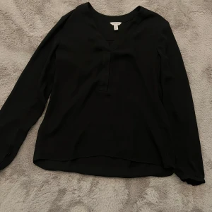 Svart blus från Calvin Klein - Elegant svart blus från Calvin Klein i storlek XS. Blusen har en v-ringad design och långa ärmar, perfekt för en stilren look. 