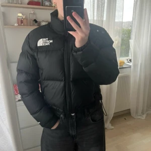 Svart dunjacka från The North Face - Säljer en svart pufferjacka från The North Face. Jackan har en dragkedja framtill och är långärmad. Perfekt för kyligare väder med sin varma och vadderade design.