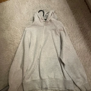 Grå hoodie - Säljer en bekväm grå hoodie med dragkedja och ficka framtill. Perfekt för kyliga dagar med sin mjuka insida och justerbara huva.