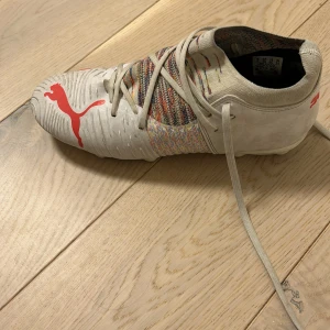 Vita fotbollsskor från Puma - Säljer ett par vita fotbollsskor från Puma med röd logga och snörning. Skorna har en färgglad detalj på ovansidan och är designade för optimal prestanda på planen.