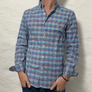 Rutig skjorta från Ralph Lauren - Säljer en snygg rutig skjorta från Ralph Lauren i blått, grönt och rött. Skjortan har långa ärmar och knappar hela vägen ner. Perfekt för både vardag och fest!