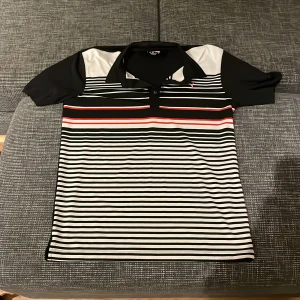 Randig pikétröja från Puma - Säljer en snygg randig pikétröja från Puma i svart, vit och röd. Perfekt för både vardag och träning. Tröjan har korta ärmar och en klassisk krage med knappar. Den är i mycket bra skick och redo för nya äventyr! Pris går alltid att förhandlas!