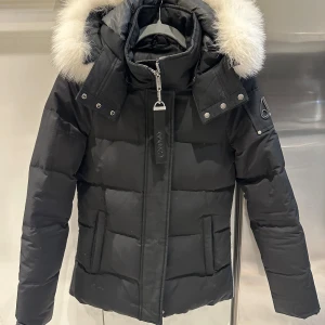 Svart dunjacka från Moose Knuckles - Snygg svart dunjacka från Moose Knuckles med pälskantad huva och dragkedja framtill. Storlek S ordinariepris 11000