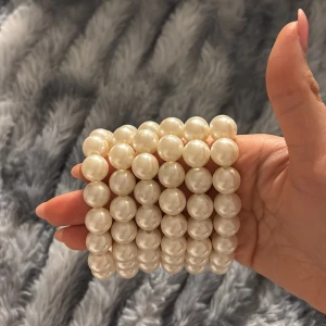 Vitt pärlarmband - Elegant vitt pärlarmband med flera rader av glänsande pärlor. Perfekt för att ge en klassisk touch till din outfit. Armbandet är elastiskt och passar de flesta handleder.