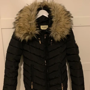 Svart pufferjacka med pälsdetaljer från Roco Baroco - Säljer en snygg svart pufferjacka från Roco Baroco i storlek 34 som är nästan oanvänt,är bara använt ett fåtal gånger och ser ut som ny. Jackan passar perfekt nu till vintersäsongen. Orginalpris:2500kr
