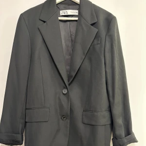 Svart kavaj från Zara - Elegant svart kavaj från Zara med klassisk design. Kavajen har två knappar framtill och fickor med lock. Str 36 aldrig använd 