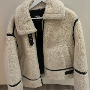 Vit teddyjacka från Zara - Mysig vit teddyjacka från Zara med svarta detaljer. Jackan är perfekt inför vintern. Köpt för en vecka sen, de blev fel storlek så knappt användts. Pris kan absolut diskuteras vid snabb affär