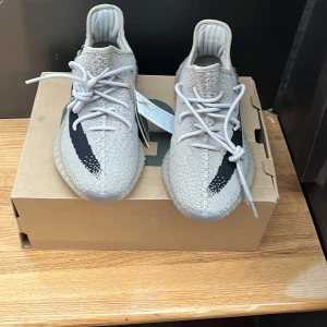 Adidas Yeezy Boost 350 V2 - Säljer ett par Adidas Yeezy Boost 350 V2 i beige med svart rand och texten 'SPLY-350'. Skorna är i mycket bra skick och har en bekväm passform med snörning.  Helt nya ej använda, endast testade. Givetvis är de äkta