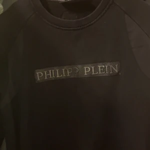 Svart tröja från Philipp Plein - Snygg svart tröja från Philipp Plein med logotyp framtill och ett litet emblem på baksidan. Perfekt för en stilren look.