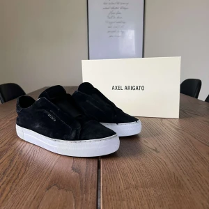 Svarta sneakers från Axel Arigato - Säljer ett par stilrena svarta sneakers från Axel Arigato. De är i mocka med en vit sula som ger en snygg kontrast. Skorna är i bra skick och kommer med originalförpackning. Hör av dig vid frågor! 