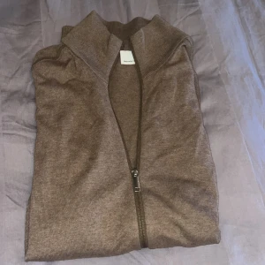 Brun full zip från Selected Homme - Säljer en snygg brun full zip från Selected Homme. Passar bra till både vardag och lite mer uppklädda tillfällen. Felfri förutom att lappen har lossnat på ena sidan (bild 2). Storlek L men passar även M