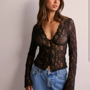 Svart spetstopp - Snygg svart spetsblus med knappar framtill och v-ringad design. Populär och slutsåld från Nelly🖤