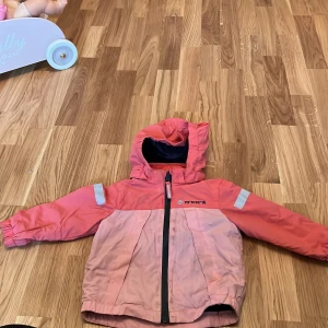 Rosa och röd jacka från H&M - Säljer en söt rosa och röd jacka från H&M med huva och dragkedja. Jackan har reflexdetaljer på ärmarna och är perfekt för små äventyrare. Passar barn i storlek 74/80.