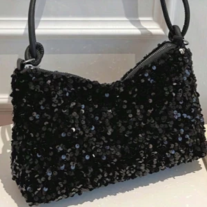 Svart paljettväska - Snygg svart axelväska täckt med glittrande paljetter. Perfekt för att ge en festlig touch till din outfit. Väskan har en dragkedja för säker förvaring och en bekväm axelrem.