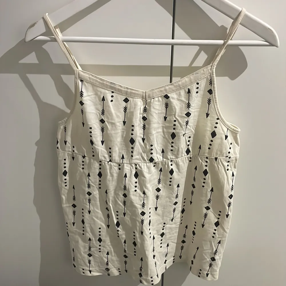 Snygg vit linne med smala axelband och ett stilrent pilmönster i svart. Perfekt för varma sommardagar eller under en kofta. Lik Brandy Melville .. Yläosat.