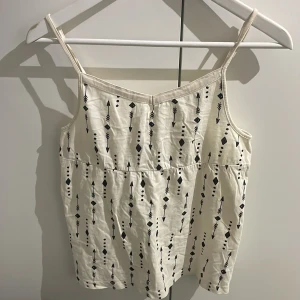 Vit linne med mönster - Snygg vit linne med smala axelband och ett stilrent pilmönster i svart. Perfekt för varma sommardagar eller under en kofta. Lik Brandy Melville .