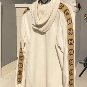 Vit hoodie från Gucci - Säljer en  vit hoodie från Gucci med bruna logotypband längs ärmarna. Använt ett par gånger men fortfarande bra skick. Pris kan diskuteras 