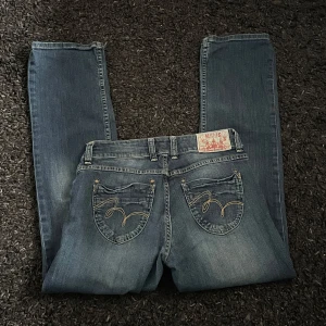 Blå jeans med broderade fickor - Säljer ett par snygga lågmidjad blå jeans med utsvängda ben, broderade detaljer på bakfickorna från nån bastille by the bay. 