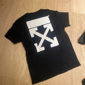 Svart t-shirt från Off-White - Säljer en svart t-shirt från Off-White i 100% bomull. Den har en ikonisk vit logga på ryggen och en liten logga på bröstet. Perfekt för en casual look eller streetwear-stil. T-shirten är i bra skick och passar till många olika outfits.
