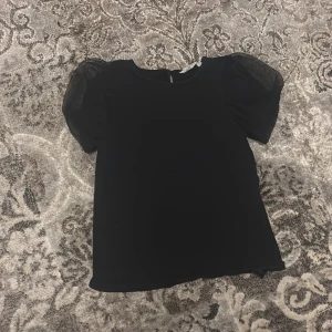 Svart topp med puffärmar - Snygg svart topp med puffiga, transparenta ärmar i mesh. Perfekt för en stilren look med en twist. Passar bra till både jeans och kjol.