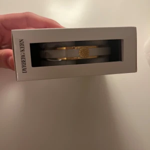 Armband från Dyrberg/Kern - Elegant armband från Dyrberg/Kern i guld och vitt. Armbandet har en stilren design med en rund gulddetalj i mitten. Perfekt för att ge en lyxig touch till din outfit. Säljer den pga stor storlek  . Fick i present helt ny oanvänd 