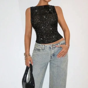 Svart glittrig ärmlös topp - Snygg svart ärmlös topp med glittriga detaljer. Perfekt för en utekväll eller fest. Den har en tight passform som framhäver figuren.