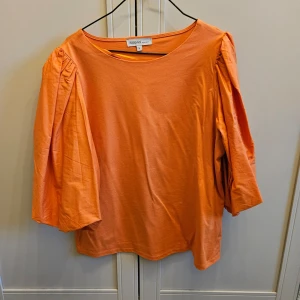 Orange topp från KappAhl i storlek S  - Säljer en snygg orange topp från KappAhl med trekvartsärmar och puffiga detaljer. Perfekt för att liva upp garderoben med en färgklick. Toppen är i en bekväm passform och tillverkad i mjukt material.