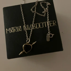 Maria Nilsdotter halsband  - Säljer mitt Maria Nilsdotter rebel love halsband med ett rött/svart hjärthänge med en pil. Halsbandet var i guld men har tappat nästan all färg så jag skulle säga att den är silvrig men de går att lämna in hos MN och doppa den. Längd på kedjan 45 nypris 4995kr.❤️