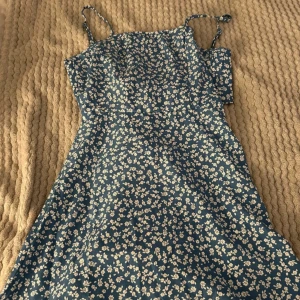 Blommig sommarklänning med smala axelband - Säljer en superfin blommig klänning i blått med små vita blommor. Den har smala axelband och är perfekt för sommar. Klänningen är i bra skick och passar både till vardags och festligare tillfällen
