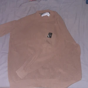 Beige tröja från Calvin Klein Jeans - Säljer en snygg beige tröja från Calvin Klein Jeans i storlek L. Tröjan är i nytt skick och har en stilren design med ribbad struktur. Perfekt för höst och vår, med långa ärmar och en bekväm passform. Ett måste för garderoben!