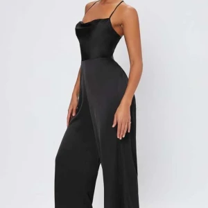 Svart byxdress - Snygg svart byxdress, rätt långa ben på den så perfekt om man är lång, silkes liknanade material. Snörning i ryggen som går att knyta på olika sätt. Storlek S, använd fåtal gånger, nyskick.