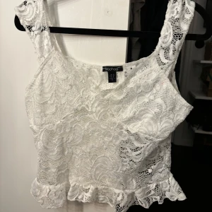 Vit spetslinne från Boohoo - Säljer ett vackert vitt spetslinne från Boohoo. Linnet har breda axelband och en fin volangdetalj vid nederkanten. Perfekt för en somrig look eller en festlig kväll. 🕊️ Storlek M! Lite rosa märken som borde gå bort i tvätten!