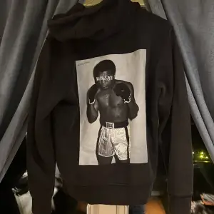 Snygg svart hoodie med ett stort tryck av Mohamed Ali på ryggen. Märket är iconsliving och den är 9/10 skick    Ny pris 600kr pris kan diskuteras 