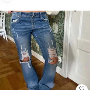 Blå slitna jeans - Säljer ett par blå jeans med slitningar på knäna och låren. De har en klassisk femficksdesign och en bekväm passform. Perfekta för en avslappnad stil och kan matchas med nästan vad som helst. Passar både till vardags och fest!