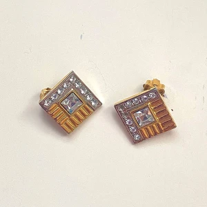 Kvadratiska clipsörhängen med kristaller - Snygga kvadratiska örhängen i guld och silver med glittrande kristaller. Vintage. De har en elegant design med en central fyrkantig sten omgiven av mindre stenar. Perfekta för att ge en touch av glamour till din look. Två stenar fattas. 