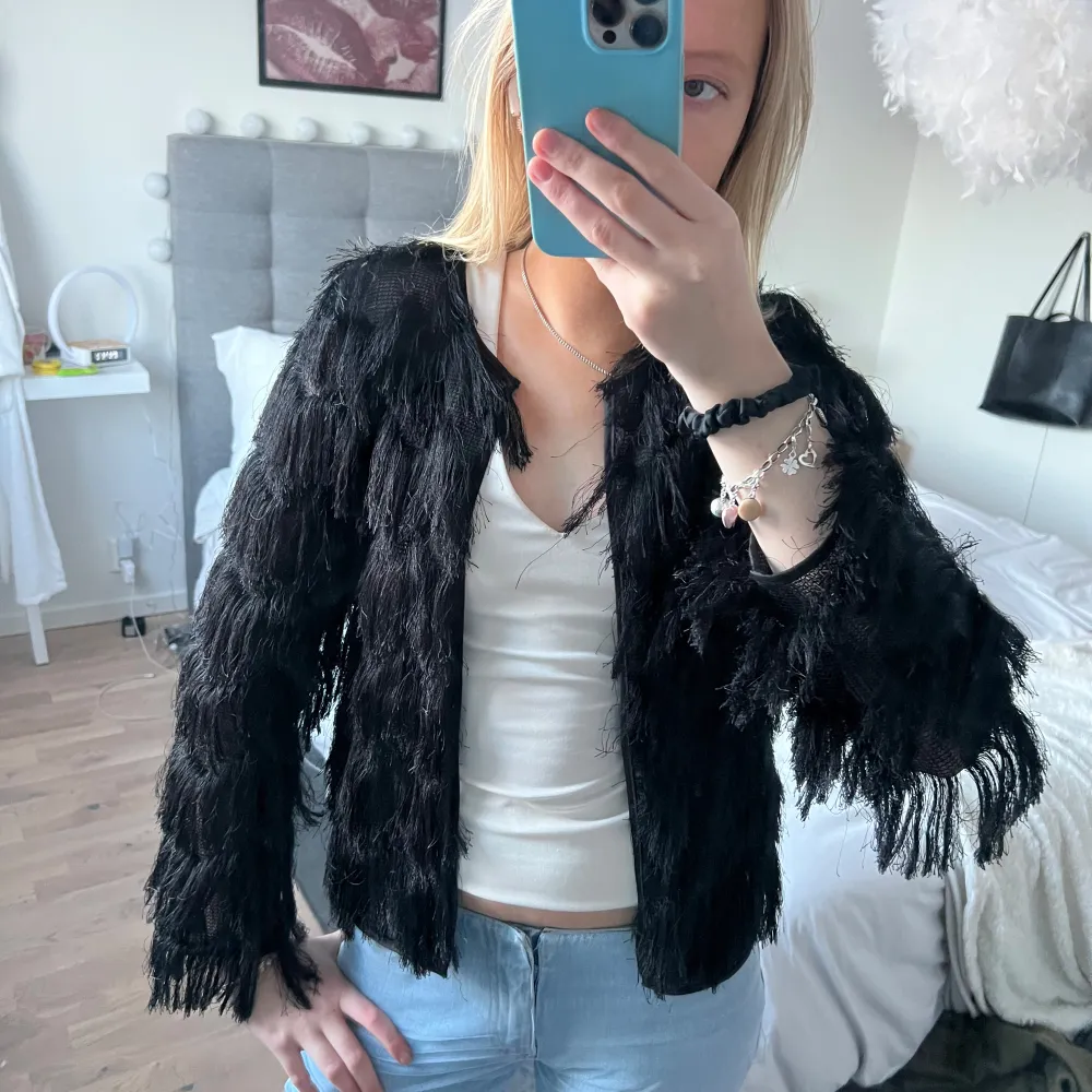 Snygg svart kofta med fransar som ger en cool och unik look. Perfekt för att sticka ut i mängden. Koftan har långa ärmar och en öppen design framtill. Passar mig som är en S!. Neuletakit & Villapaidat.