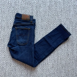 Nudie Jeans - Säljer ett par snygga mörkblå jeans från Nudie i modell Brute Knut. Jeansen är i riktigt bra skick och har inga tecken på användning förutom att läderpatchen är lite skrapad men inget som märks. Det är storlek W28/L30. Vid minsta fråga eller fundering är det bara att höra av sig👍😁