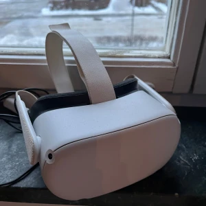 Oculus quest 2 VR-headset - Säljer ett stilrent vitt VR-headset med justerbart huvudband. Perfekt för att dyka in i virtuella världar och uppleva spel och filmer på ett helt nytt sätt. Enkel att använda och bekväm att bära under längre sessioner. Kommer med linkcabel. Nypris för headsetet och cabeln är runt 4000kr