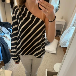 Svart och vit randig oneshoulder topp - Snygg svart och vit randig oneshoulder topp med långa ärmar. Perfekt för en trendig look med en unik asymmetrisk design.